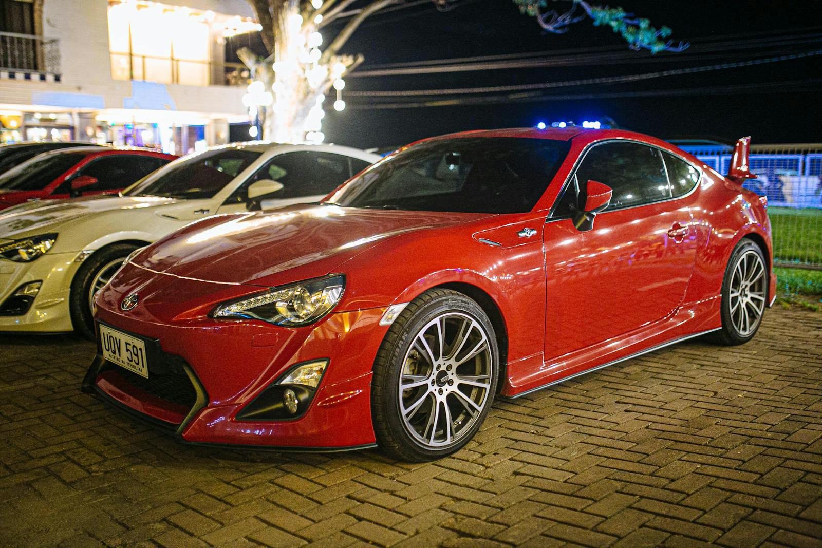A sleek red sports car nicely illuminated, parked on paved road at night in the Philippines.
